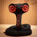 Load image into Gallery viewer, MM Figur Sacky Serpent (13 cm) er et sammenrullet, sort plysdyr med røde knapøjne og syede "X"er, perfekt som samlerfigur eller unik pynt til hylden, vist på en træbaggrund.