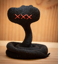 Load image into Gallery viewer, MM Figur Sacky Serpent (13 cm) er en sammenrullet sort strikket figur med tre røde syede X-øjne, der vises på en træoverflade som en iøjnefaldende samlerfigur og pynt til hylden mod en sløret træbaggrund.