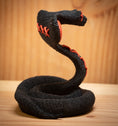 Load image into Gallery viewer, MM Figur Sacky Serpent (13 cm) er en sort, sammenrullet voodoo-slangefigur med røde syninger, der står oprejst på en træplade - perfekt som hyldeudsmykning.