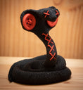 Load image into Gallery viewer, MM Figur Sacky Serpent (13 cm) er en sammenrullet sort figur med røde knapøjne og syede X-mærker, der står oprejst - ideel som hyldeudsmykning.
