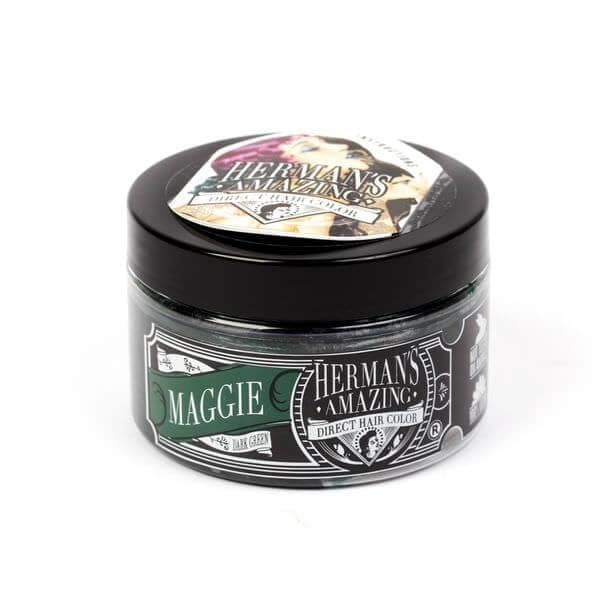 En sort, rund plastikbeholder mærket "Hermans Hårfarve Maggie (115ml)" af Hermans har et vintage-stilbillede af en kvinde i en hat på låget. Denne veganske hårfarve giver levende farver med et miljøvenligt touch.